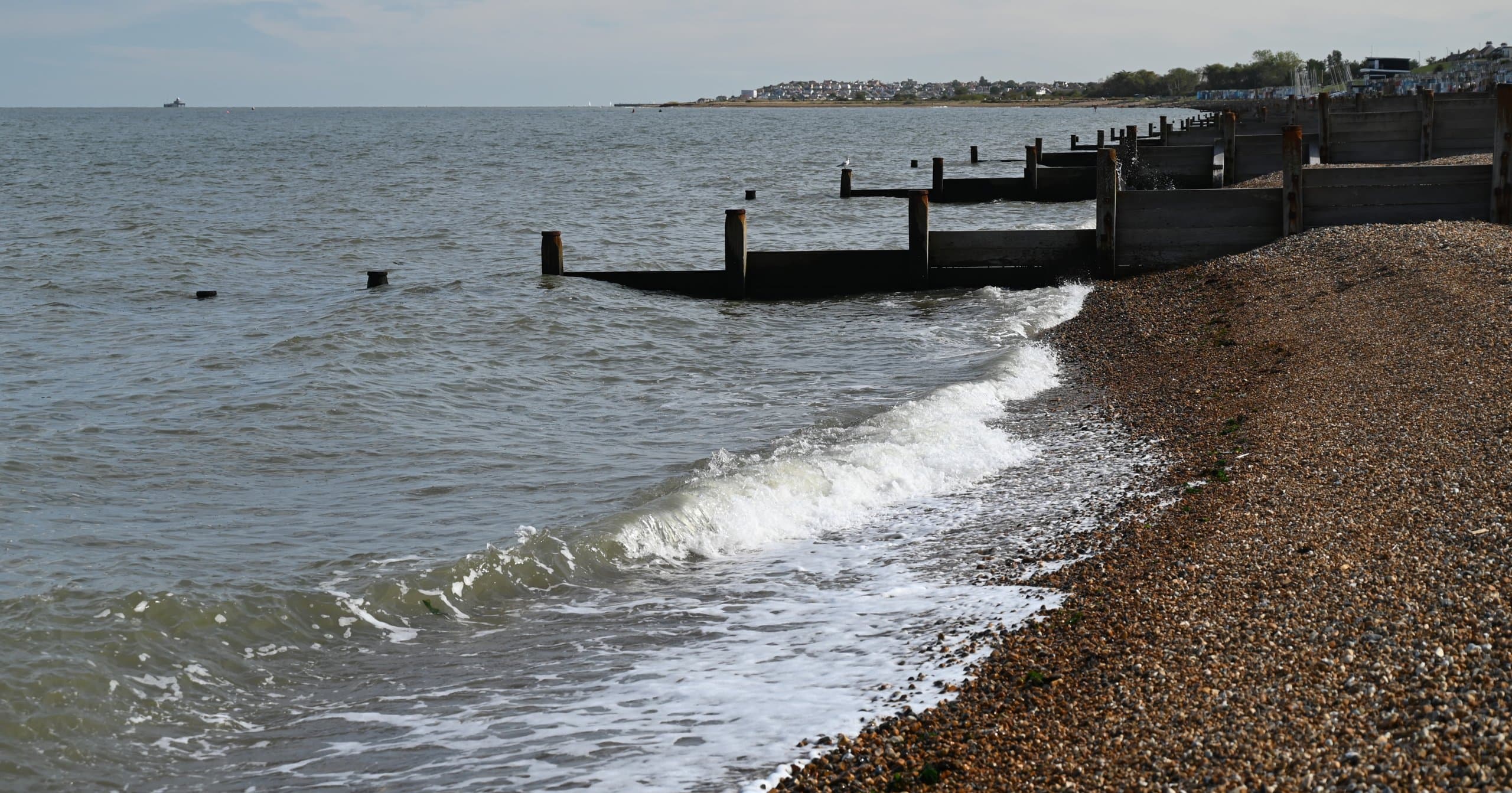 Waves breaking along a shingle beach with wooden groynes
